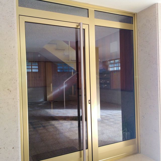 Puerta de portal em imitación oro con tirador en inoxidable instalada en Suances Cantabria
